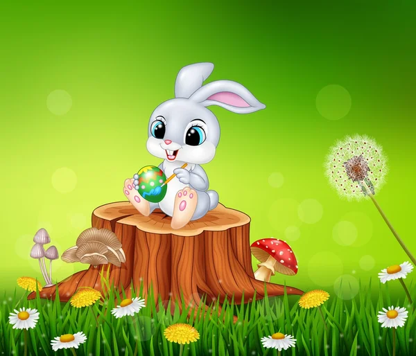Dibujos animados Conejo de Pascua pintando un huevo en el tocón del árbol en el fondo de temporada de verano — Vector de stock
