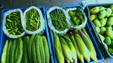 Farklı sebzeler ve mısır koçanının üzerinde kabuğu bir dükkandaki tepsilerde çeşitli ürünler sunuyor. Sahne, yerel üretimin tazeliğini vurguluyor.