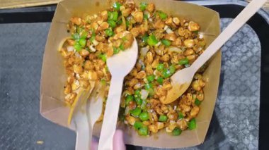 Yeşil fasulye ve sosla gevrek mısır sohbeti bir tabakta sunuluyor, insanlar yerken iki kaşık topluyor..