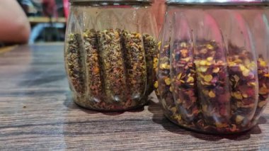 Arka planda insanların oturduğu fıskiye şişelerindeki karışık pizza çeşnilerinin yakınlaştırılması,.