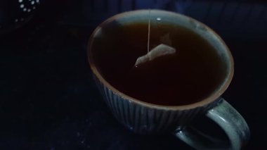 Çay poşeti siyah çay demlemek için bir bardak suya batırılır, çay yapma sürecini betimler..