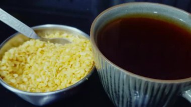 Çelik bir kasenin içinde, sıcak bir içecekle lezzetli atıştırmalıkların karışımının yanında siyah çay servis edilir..