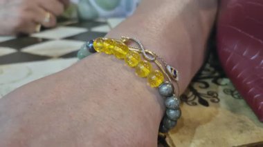 Bir kadının elinde çok renkli boncuk bilezikler ve basit tasarım ve metalik parlaklığı birleştiren altın bir bilezik bulunur..