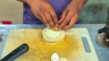 Bir adam üzerine dilimlenmiş domates ve kapsiyum koyarak peynirli burger hazırlar. Renkler ve taze malzemelerin dokularını birleştirir..