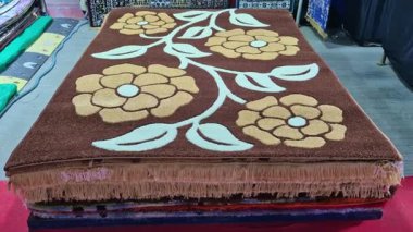 Satılık halı ve halılar sergileniyor, bazıları yığınlar halinde katlanmış, bazıları ise doku ve renk kalıplarını göstermek için asılıyor..