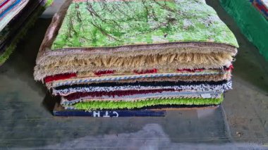 Yığılmış renkli halı ve halılar katmanlı bir düzenleme oluşturuyor. Ayrıntılı desenleri ve kumaş dokularını gösteriyor..