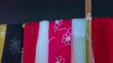 Chunni, eşarp ve parlak renkli sariler gece pazarında sergilenir. Kumaş desenlerini yansıtan yumuşak ışıklarla aydınlatılır..