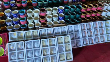 Yol kenarındaki panayır yerinde renkli bardaklar ve tabaklar sergileniyor, gölgelerde çeşitlilik gösteriliyor ve bitiriliyor.