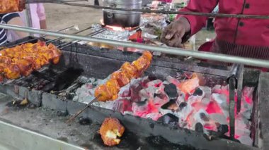 Kömür ve ateş kavrulurken kebapları hareket ettiren bir şefin yakın görüntüsü yemek pişirme sürecini ayrıntılı olarak gösteriyor..