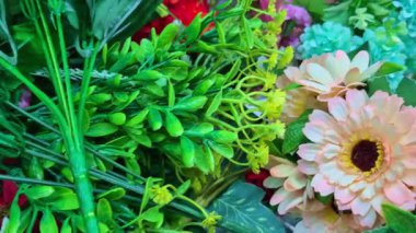 Çeşitli renkli sahte çiçekler ve yeşil saplar bir mağazada satışta sergilenmekte ve karışık tasarımlar sunulmaktadır..