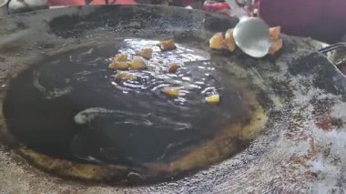 Bir adam, yol kenarındaki tipik bir yemek takımını göstererek, görünürde kirli yağda patates kızartması yapar..