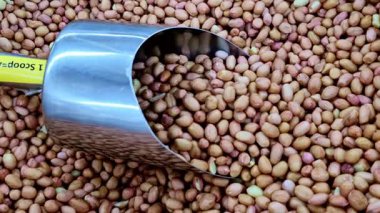 Yakın çekim görüntüsü, yoğun bir yuvarlak, açık kahverengi Peanut yığını arasında, düz mat yüzeyleri ve hafif renk değişimleriyle yan yana dizilmiş metal bir kepçeyi gösterir..