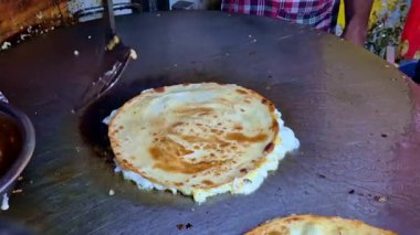Bir tarafında taze pişmiş yumurta paratha ile büyük bir sokak-yiyecek ızgarası yakın çekim, merkezinde koyu bir ısı işareti, ve arka planda görünen sebzeler doğranmış.