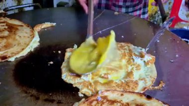 Sıcak, düz bir ızgara üzerinde yeni pişirilmiş yumurta, tereyağı veya yağ gibi metal bir spatula ile çevrilmiş, altın-kahverengi katmanlar ve çıtır çıtır kenarları gösteren yakın plan..