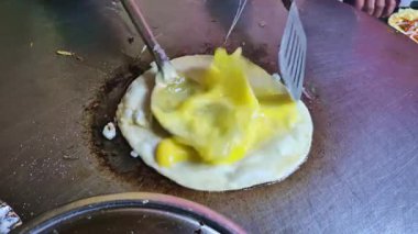 Metal bir spatula, iki kırık yumurta sarısını ısıtılmış ızgarada pişerken yuvarlak ekmeğin yüzeyine yayar..