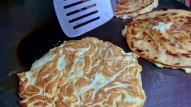 Ekgroll paratha sıcak ızgara pişirirken yakın plan yumurta akı, görünür yumurta sarısı ve başka bir yumurta paratha yanında altın-kahverengi çıtır ekmek gösterilir..