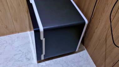 Gümüş bukleli kompakt siyah bir buzdolabı görünür güç kablolarıyla ahşap bir duvara dayanır ve döşeme döşemesi kullanışlı bir iç tesisatı vurgular..