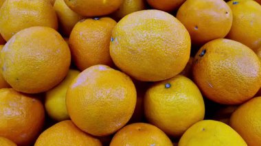 Pazar yerinde bir araya toplanmış taze portakal yığını gamzeli desenli parlak portakal kabuklarını ve yumuşak gün ışığı altında doğal yüzey değişimlerini gösteriyor..