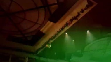 Canlı bir görüntü, karanlık bir kapalı alanda, kıvrımlı bir tavan boyunca uzanan mavi ve yeşil lazer ışınlarının kesiştiğini gösteriyor. Işık sisi ışığın görüş mesafesini arttırıyor ve dramatik, daldırıcı bir atmosfer yaratıyor..