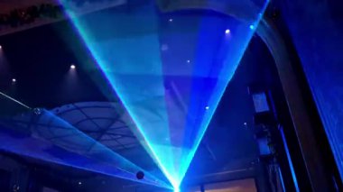 Canlı bir görüntü, mavi, yeşil ve kırmızı lazer ışınlarının kesiştiği geniş kemerli tavanın altındaki sisi keserken sahne aydınlatması ve mimari detaylarla kapalı mekanda yüksek enerjili bir konser atmosferi yaratıyor..