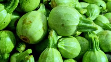 Yakın plan taze meyve (Hint yuvarlak sukabağı) sebzeleri bir market tezgahında üst üste yığılmış, dolgun yeşil gövdeler, kısa gövdeler ve taze hasat ve tazeliği gösteren pürüzsüz derileri göstermektedir.