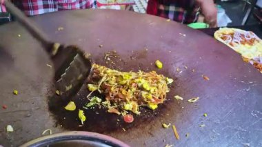 Değişik renkte sebzeler ve yiyecek artıkları büyük, düz bir metalik ızgara yüzeyine dağılmış, koyu, dairesel ısı kararmış bir bölge etrafında yoğunlaşmıştır..