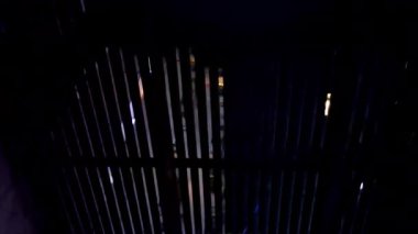 Işık, karanlık, dekolteli bir yapıdan geçer. Muhtemelen metal bir kapı ya da pencere. Neredeyse tamamen siyah bir arkaplana karşı dar dikey ışık çizgileri oluşturur..