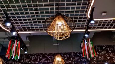 Örülmüş rattan kolye lambaları ve parlak yol ışıklarıyla modern restoran tavanı. Dekoratif üç renkli flamalar beyaz ızgara tarzı endüstriyel tavanın altında asılı..