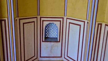 Tarihi bir Jaipur yapısındaki dekoratif bir iç duvar, delinmiş taş kafes pencereli küçük kemerli bir oyuk içerir. Güneş ışığı desenli açıklıklardan süzülerek geleneksel kırmızı kenarlı duvar tasarımını vurgular.