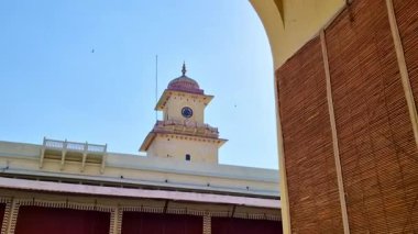 Jaipur 'un Şehir Sarayı' nın krem rengi saat kulesi parlak mavi bir gökyüzüne karşı duruyor. Sert güneş ışığı, tarihi Rajput mimarisinin yanında bir mercek patlaması yaratır..