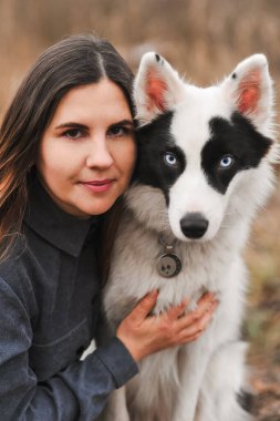 Yakutian Laika köpeğiyle birlikte doğal ışıkta genç bir kadının yakın portresi. Huzurlu bir kırsal alanda insan ve kuzey cins köpek arasında sakin bir dostluk, güven ve bağlantı gösteren duygusal bir yaşam tarzı..