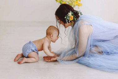 Açık mavi tül elbiseli bir anne bebeğine bakarak yerde yatıyor, merak ve duygusal bağlarla dolu samimi bir etkileşim yaratıyor. Yumuşak ışıklandırma ebeveyn ve çocuk arasındaki sıcaklığı ve yakınlığı arttırır.