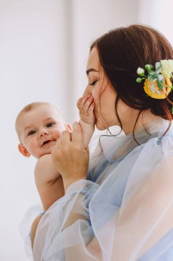 Sevgi dolu bir annenin bebeğini kucaklarken elini öptüğü yakın plan bir portre. Yumuşak doğal ışık, ebeveynler ve bebekler arasındaki duygusal bağ, şefkat ve samimiyeti ön plana çıkarır. Nazik pastel tonlar ve havadar stil sakin bir anne yaratıyor.