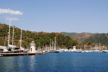 Türkiye 'de Akdeniz kıyısındaki küçük deniz feneri yakınlarında yatları ve yelkenli tekneleri olan Marina. Dağlı sakin deniz manzarası ve berrak su yaz seyahatlerini ve tatil beldeleri atmosferini temsil ediyor..