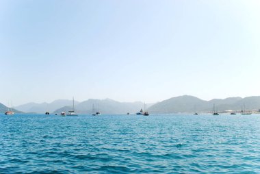 Türkiye 'nin Marmaris kenti yakınlarındaki sakin Akdeniz' e demirli yelkenliler. Berrak su ve uzak dağlarla huzurlu kıyı manzarası rahatlatıcı yaz seyahatleri ve tatil atmosferi yaratıyor..