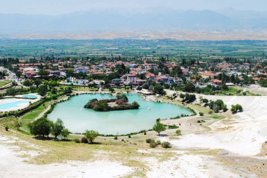Türkiye 'nin Pamukkale kenti yakınlarındaki yeşil park alanıyla çevrili turkuaz termal gölün panoramik görüntüsü arttı. Arka planda görünen doğal teraslar ve kırsal manzaralar. Termal yaylar ve manzaralı manzaralarla ünlü bir seyahat yeri..