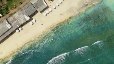 Okyanus mavi dalgalarının havadan görünüşü kumsalda kırılıyor. Deniz dalgaları ve güzel kumsal manzaralı insansız hava aracı görüntüleri. Kuş bakışı okyanus dalgaları küçük köylü kumsala çarpıyor. 