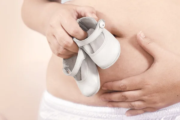 Schwangerer Bauch mit kleinen Schuhen — Stockfoto