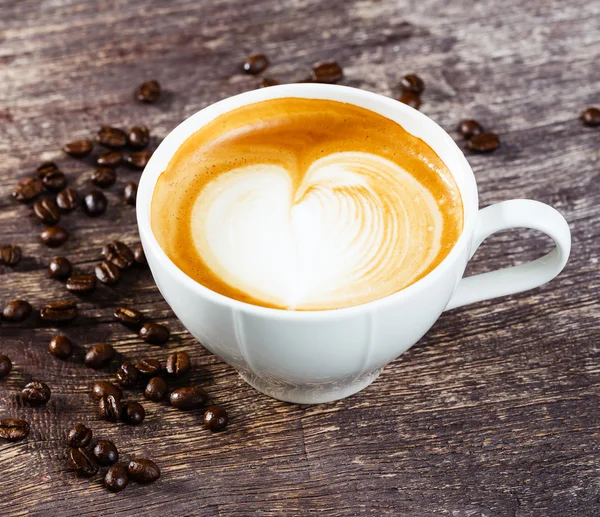 Tasse Kaffee und geröstete Bohnen auf altem Holztisch — Stockfoto