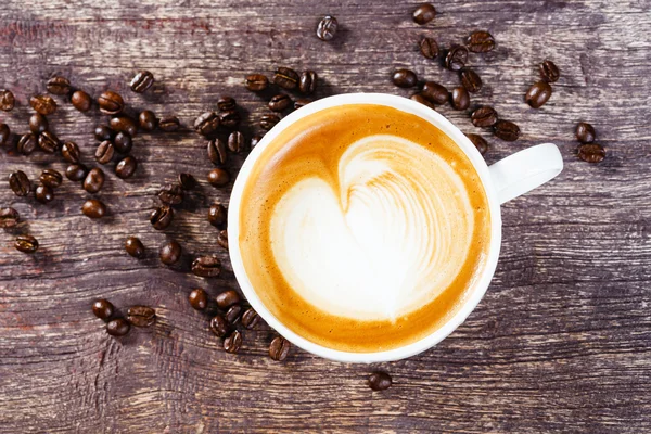 Tasse Kaffee und geröstete Bohnen auf altem Holztisch — Stockfoto