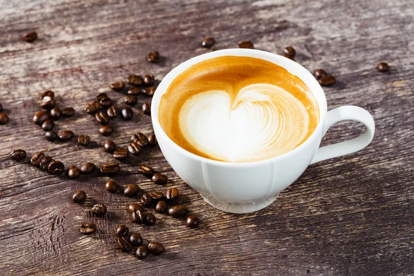Tasse Kaffee und geröstete Bohnen auf altem Holztisch — Stockfoto