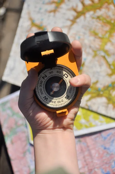 Compass in hand on a blurred background topographic maps. — Stock Photo, Image