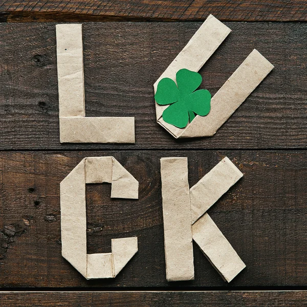 Origami de papel artesanal LUCK letras sobre fondo rústico de madera de granero oscuro. Hoja de trébol verde. Plantilla de postal de saludo del Día de San Patricio . — Foto de Stock