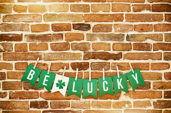 BE LUCKY banner lettering on red, old orange brick wall background. Irish national colors St. Patrick's Day greeting postcard template. Space for cope, text. — Stok fotoğraf