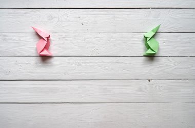 Paper origami handmade pink, green bunnies on white planks barn wood boards background. Space for text, lettering, copy. Easter holiday postcard template.