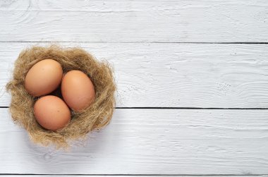Nest with eggs on white wooden planks background. Easter greeting postccard template. Space for copy, text, lettering.
