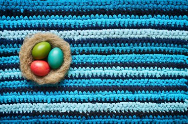 Colored Easter eggs in natural nest on cotton t-shirts upcycle handmade navy blue cyan striped rug background. Space for text, lettering, copy.