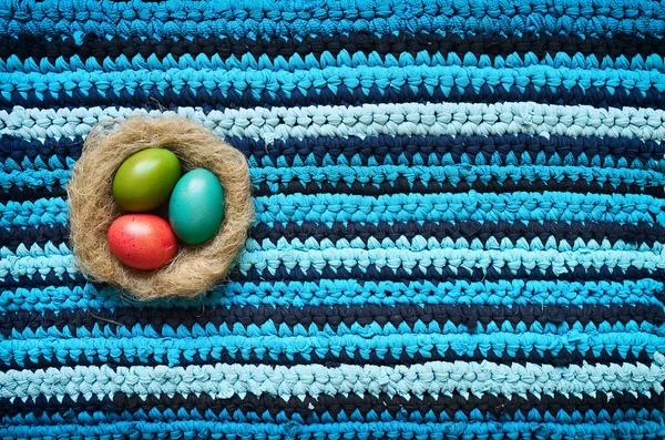 Colored Easter eggs in natural nest on cotton t-shirts upcycle handmade navy blue cyan striped rug background. Space for text, lettering, copy. — ストック写真