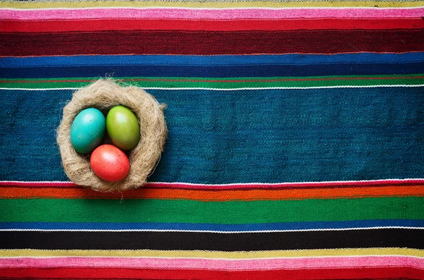 Ovos de páscoa coloridos no ninho em artesanal tradicional velho ucraniano colorido tapete listrado tapete de fundo. Espaço para texto, cópia, letras . — Fotografia de Stock