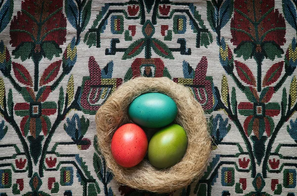 Farbige Ostereier im Nest auf floralem Stoffhintergrund. — Stockfoto